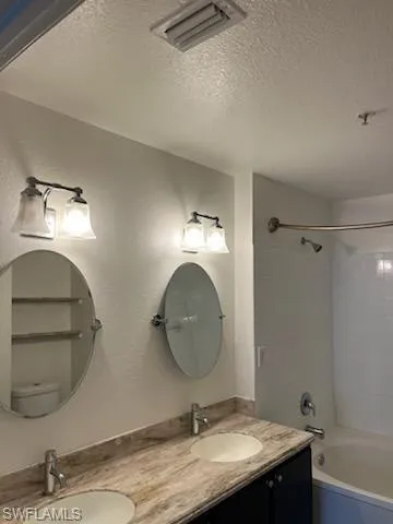 Bathroom featuring double sink vanity, tiled shower / bath combo, and a textured ceiling