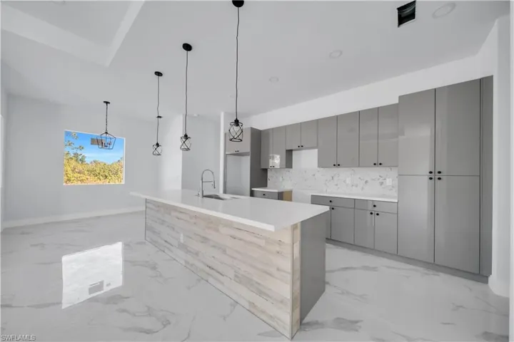 Kitchen with gray cabinetry, a center island with sink, modern cabinets, pendant lighting, and decorative backsplash