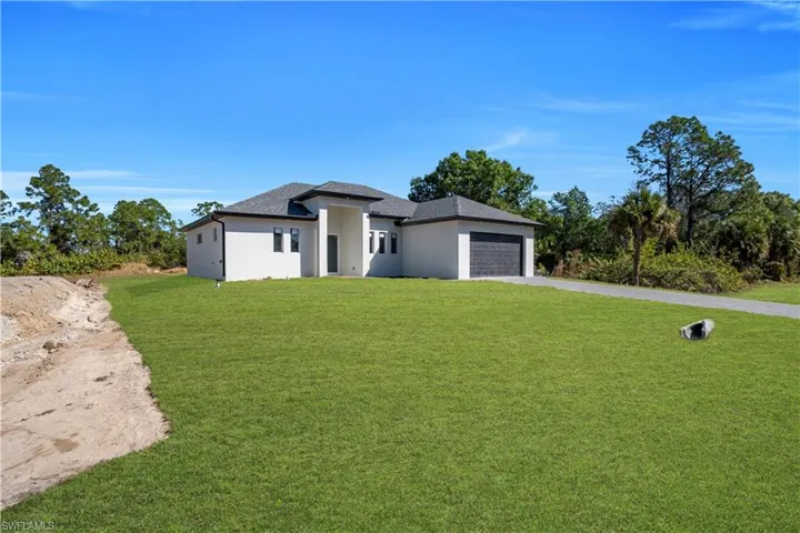 Prairie-style home featuring driveway, a front yard, an attached garage, and stucco siding