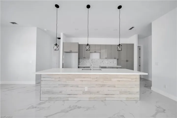 Kitchen featuring modern cabinets, a large island with sink, pendant lighting, gray cabinetry, and tasteful backsplash