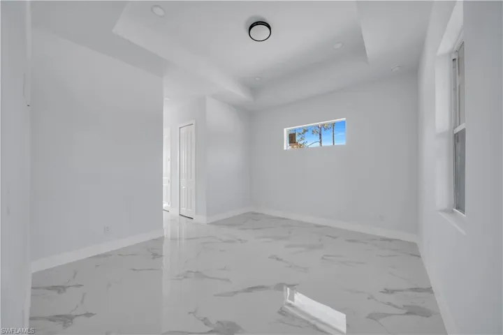 Unfurnished room featuring a tray ceiling and light marble finish flooring