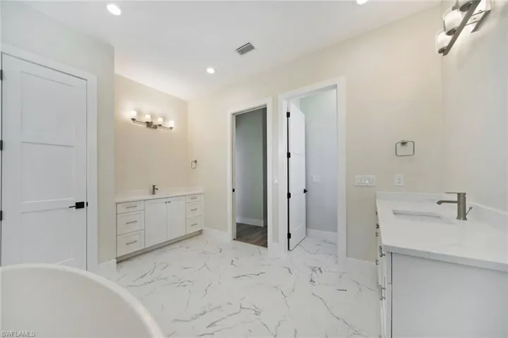 Full bathroom with two vanities, light marble finish floors, a freestanding bath, and recessed lighting