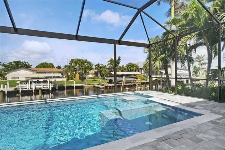 View of swimming pool featuring a water view, glass enclosure, a pool with connected hot tub, and a sunroom