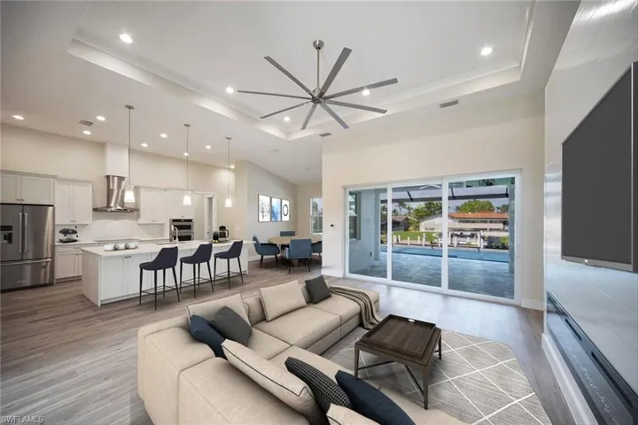 Living room featuring a tray ceiling, light wood-style floors, recessed lighting, and a high ceiling - virtually staged