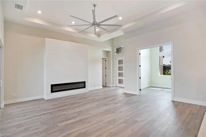 Unfurnished living room featuring a tray ceiling, light wood-type flooring, a glass covered fireplace, recessed lighting, and a ceiling fan