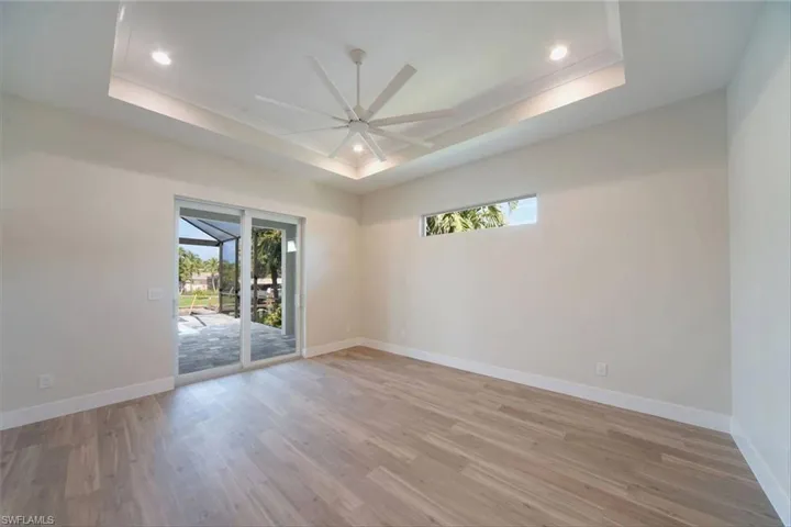 Empty room featuring a raised ceiling, light wood finished floors, recessed lighting, and ceiling fan