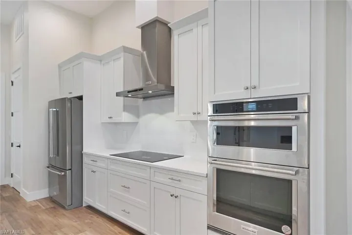 Kitchen with appliances with stainless steel finishes, wall chimney range hood, white cabinetry, and light wood-type flooring