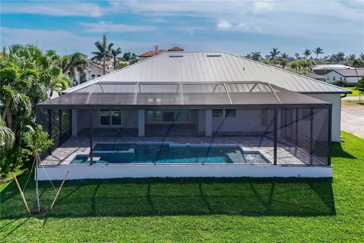 Rear view of property featuring glass enclosure, a sunroom, a lawn, and a pool with connected hot tub