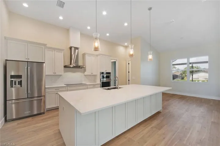 Kitchen with appliances with stainless steel finishes, white cabinets, wall chimney range hood, pendant lighting, and light wood-type flooring
