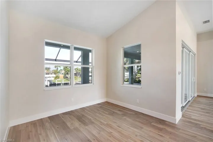 Unfurnished room with healthy amount of natural light, light wood-style flooring, and vaulted ceiling