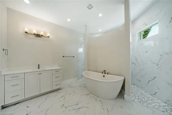Bathroom featuring vanity, a freestanding tub, a marble finish shower, recessed lighting, and light marble finish floors