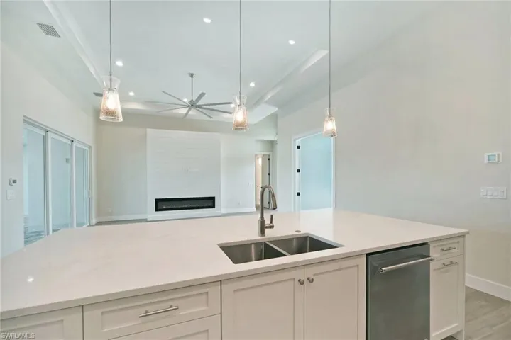 Kitchen with white cabinetry, open floor plan, pendant lighting, light stone counters, and a glass covered fireplace