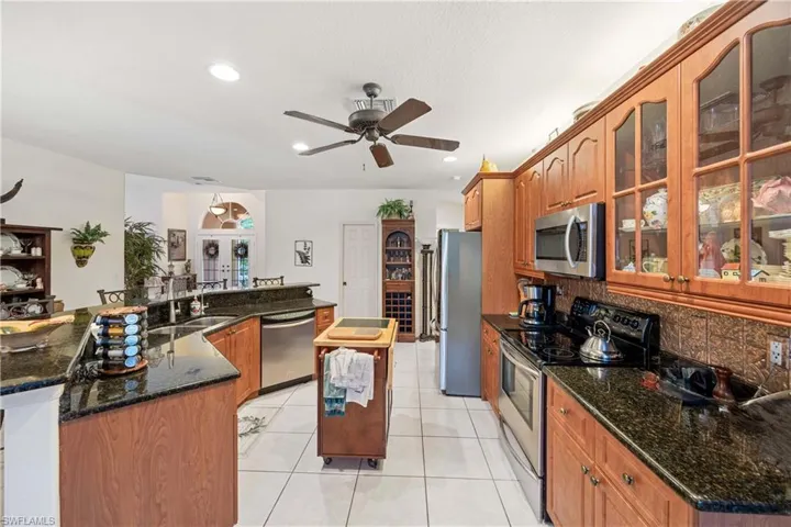 Kitchen with appliances with stainless steel finishes, a spacious island, tasteful backsplash, light tile patterned flooring, and glass insert cabinets