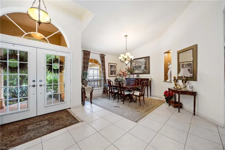 Dining area with a chandelier, light tile patterned floors, french doors, and high vaulted ceiling
