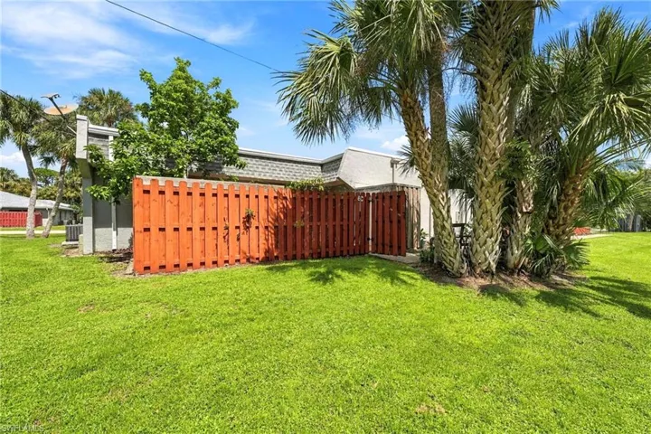 Exterior area featuring a fenced side yard with mature palm trees and green lawn