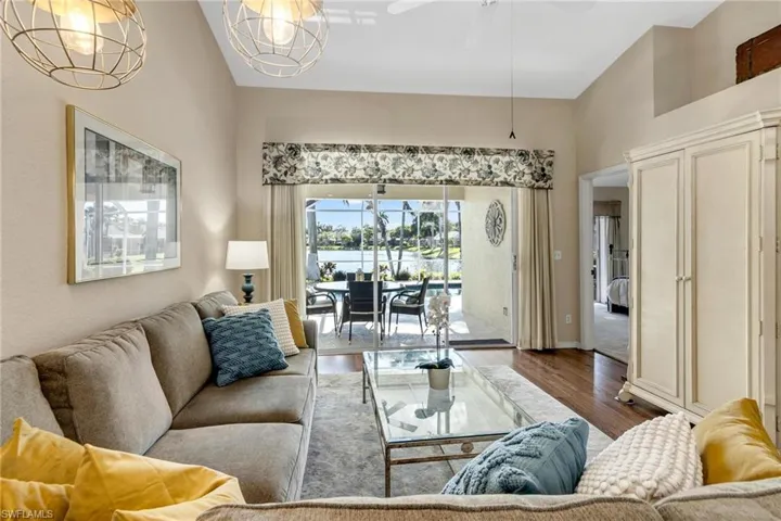 Living room featuring vaulted ceiling, a healthy amount of sunlight, ceiling fan with notable chandelier, and dark hardwood / wood-style floors