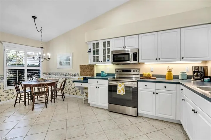 Kitchen with appliances with stainless steel finishes, decorative light fixtures, lofted ceiling, and white cabinets