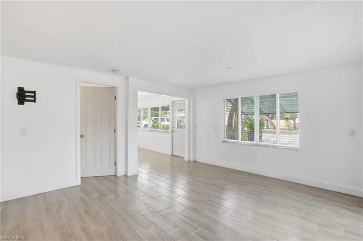 Spacious room featuring light wood-finish flooring, white walls, and a large window with horizontal blinds - Virtually Edited Image
