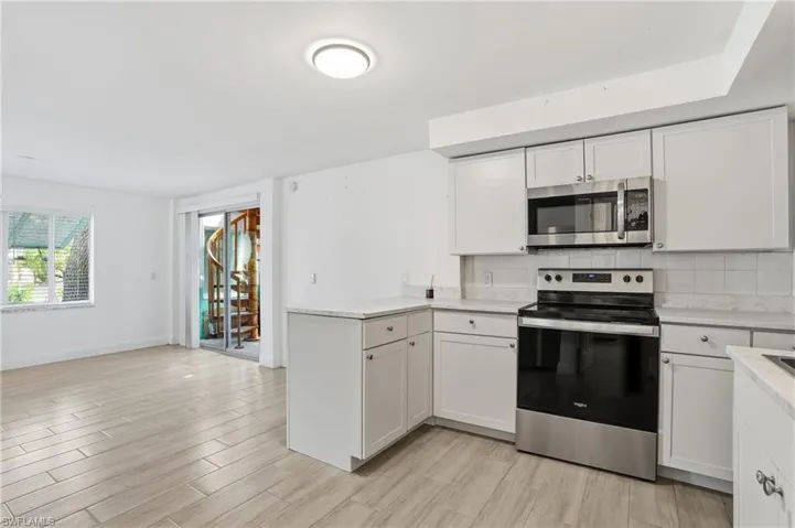 Bright kitchen area featuring white shaker-style cabinetry, light-toned countertops, a stainless steel range, and an over-the-range microwave - Virtually Edited Image