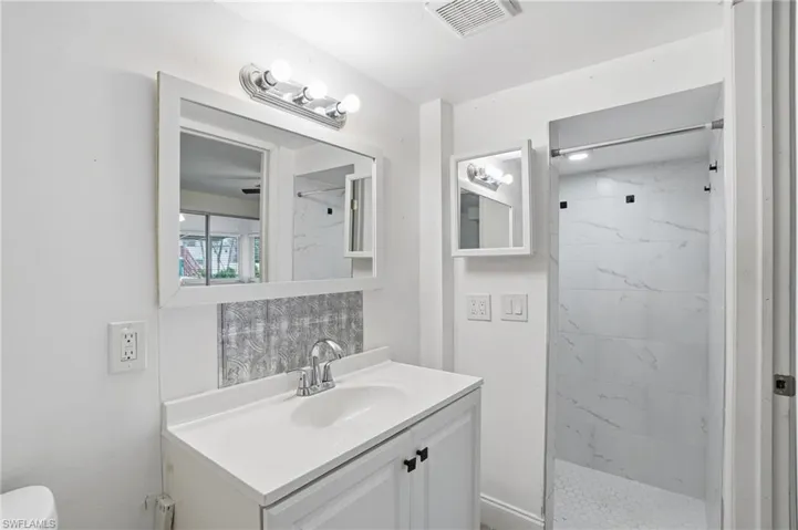 Bathroom featuring a white vanity with integrated sink, chrome faucet, and overhead vanity lighting - Virtually Edited Image