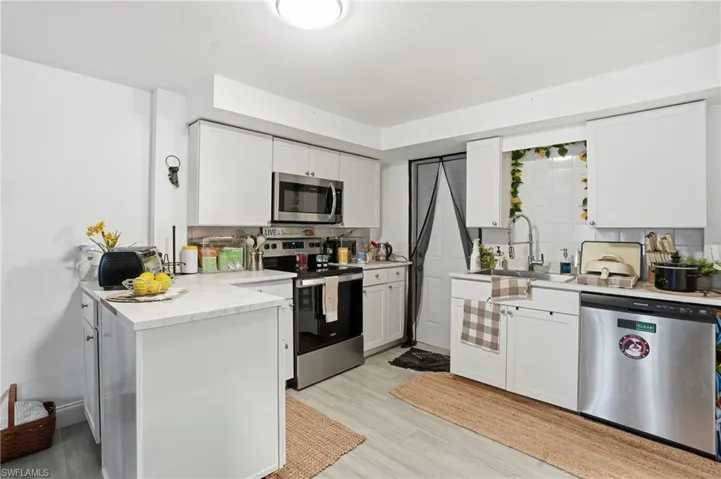 Kitchen featuring appliances with stainless steel finishes, a peninsula, white cabinetry, tasteful backsplash, and light wood-style flooring - Virtually Edited Image