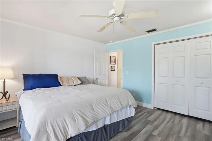 Bedroom with crown molding, wood finished floors, a ceiling fan, a closet, and wooden walls - Virtually Edited Image