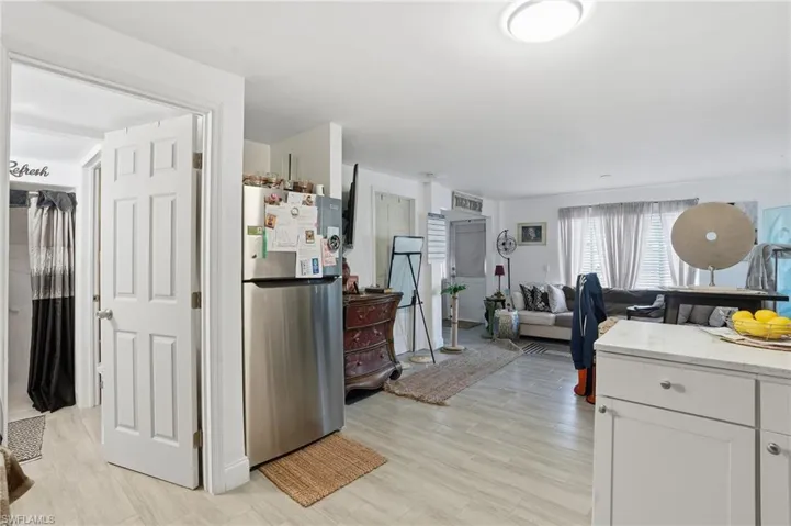 Kitchen with freestanding refrigerator, light stone counters, white cabinets, light wood finished floors, and open floor plan - Virtually Edited Image