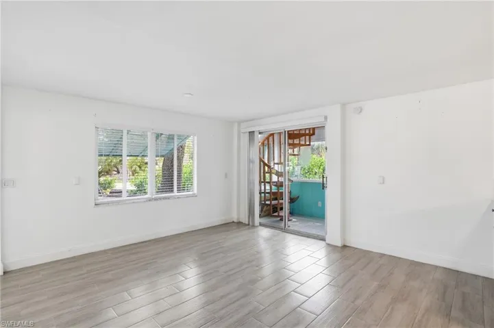 Bright interior space featuring neutral wall tones, wood-finish flooring, and a multi-pane window with horizontal blinds - Virtually Edited Image