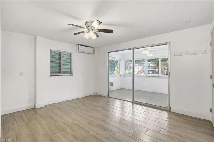 Spacious room featuring wood-finish tile flooring, a ceiling fan with integrated lighting, and a wall-mounted air conditioning unit - Virtually Edited Image