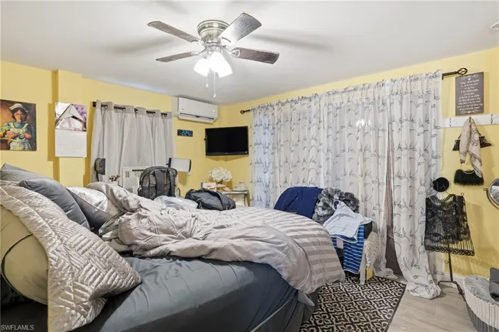 Bedroom with wood finished floors, ceiling fan, and a wall mounted AC - Virtually Edited Image