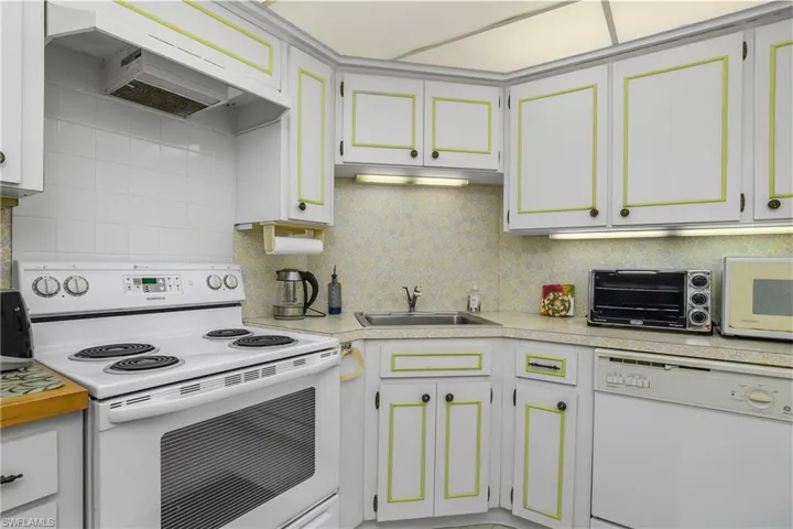 Kitchen with white appliances, premium range hood, light countertops, decorative backsplash, and white cabinetry