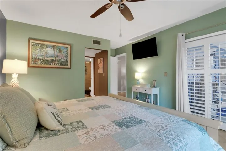 Tiled bedroom with ceiling fan, ensuite bath, and access to exterior
