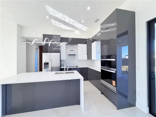 Kitchen with two tone cabinetry, modern cabinets, stainless steel appliances, light stone countertops, and a large island