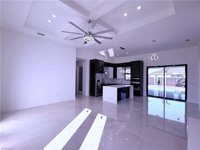 Kitchen with dark cabinetry, a kitchen island, coffered ceiling, open floor plan, and stainless steel fridge with ice dispenser