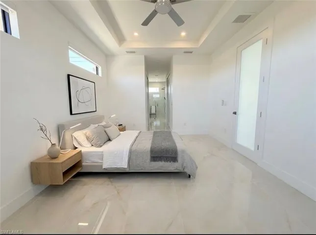 Bedroom with ensuite bath, a tray ceiling, a ceiling fan, and recessed lighting
