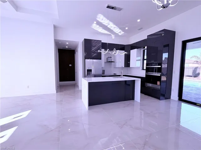 Kitchen featuring modern cabinets, stainless steel appliances, a center island with sink, light stone counters, and pendant lighting