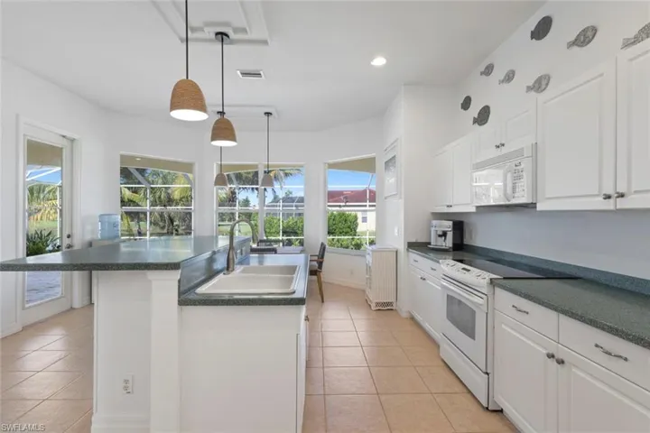 Kitchen with white cabinetry, dark countertops, white appliances, light tile patterned flooring, and recessed lighting