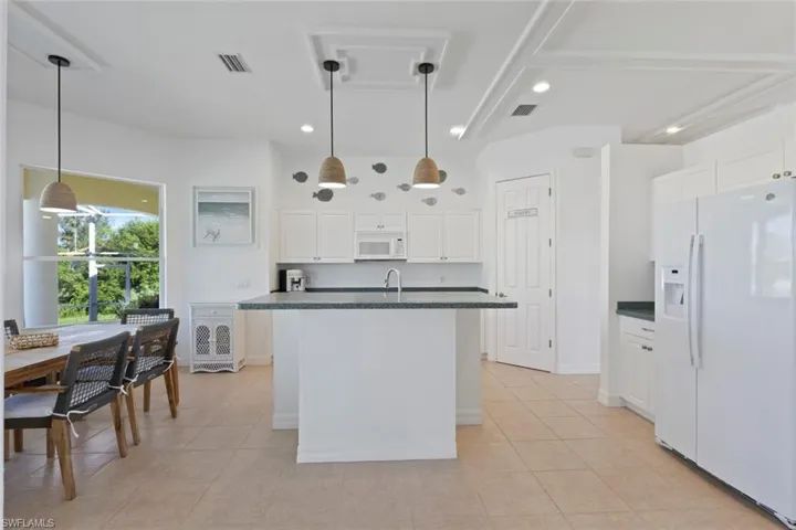 Kitchen with dark countertops, white appliances, white cabinets, a kitchen island with sink, and light tile patterned floors