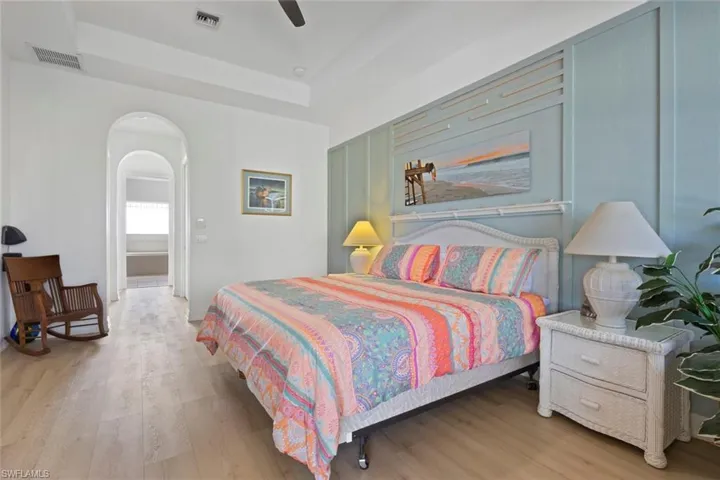 Bedroom with arched walkways, light wood-style flooring, a raised ceiling, and ceiling fan