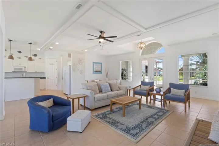 Living area with french doors, beam ceiling, light tile patterned flooring, ceiling fan, and a chandelier