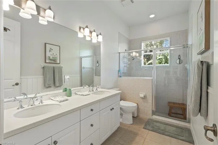 Bathroom featuring double vanity, light tile patterned floors, a shower stall, and wainscoting