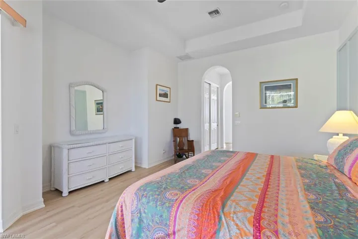 Bedroom with arched walkways, light wood-style floors, a closet, and a tray ceiling