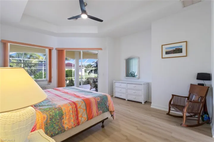 Bedroom with access to exterior, light wood-type flooring, a raised ceiling, and a ceiling fan