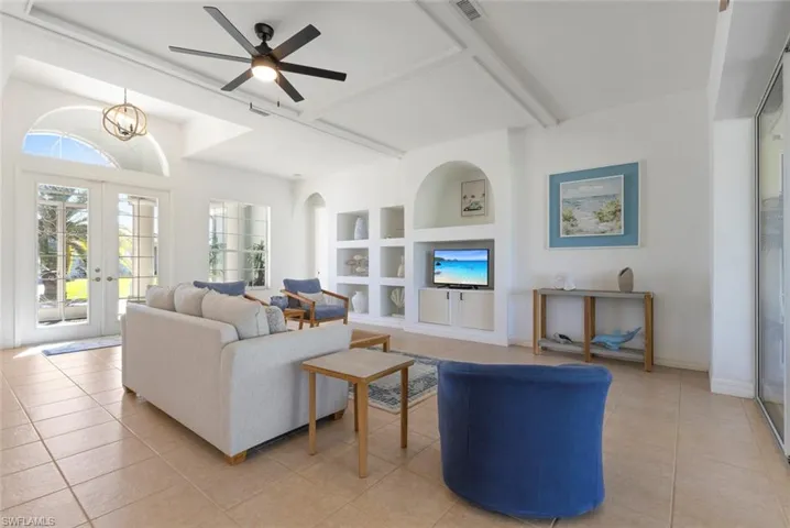 Living room with built in shelves, french doors, beam ceiling, light tile patterned flooring, and a ceiling fan