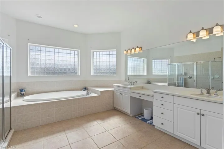 Full bathroom featuring two vanities, a bath, a shower stall, light tile patterned flooring, and recessed lighting