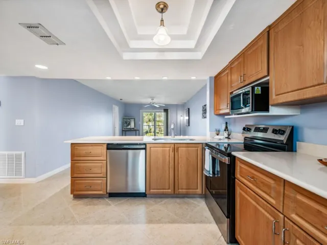 Kitchen featuring pendant lighting, sink, stainless steel appliances, a raised ceiling, and kitchen peninsula