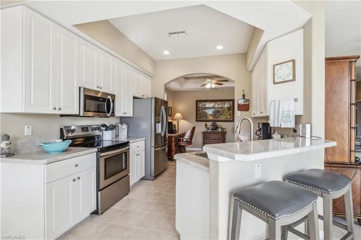 Kitchen featuring a kitchen breakfast bar, kitchen peninsula, stainless steel appliances, white cabinetry, and ceiling fan
