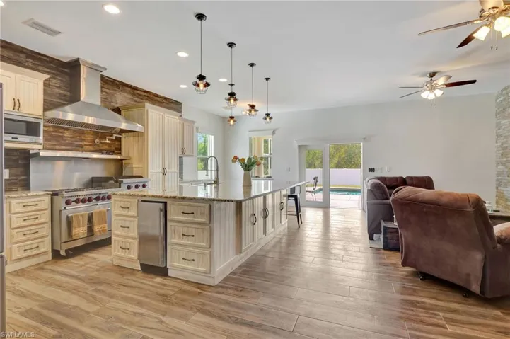 Kitchen with Chefs 6 burner Gas stove, quartz counters, stainless steel appliances, kitchen island with sink, range hood, and decorative light fixtures