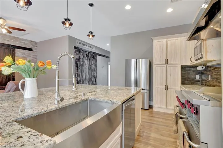 Kitchen with light stone countertops, sink, exhaust hood, and appliances with stainless steel finishes