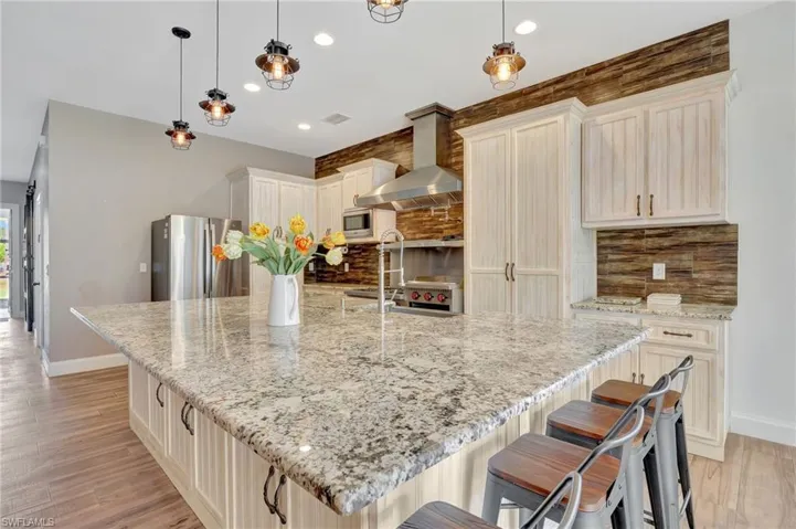 Kitchen stainless steel appliances, light stone counters, backsplash, and pendant lighting